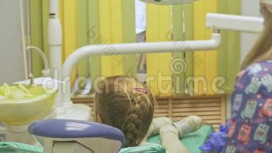 带着一个母亲的孩子在牙医`接待处。 女孩躺在椅子上，在她母亲的身后。 医生和一个